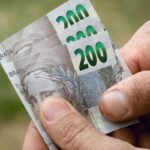 Pessoa segurando três notas de R$ 200 nas mãos, representando recebimento de dinheiro, pagamento de precatório, RPV ou antecipação de crédito.