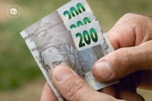 Pessoa segurando três notas de R$ 200 nas mãos, representando recebimento de dinheiro, pagamento de precatório, RPV ou antecipação de crédito.